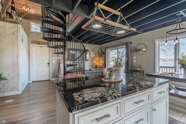 kitchen with wood finished floors, baseboards, white cabinets, open floor plan, and dark stone counters