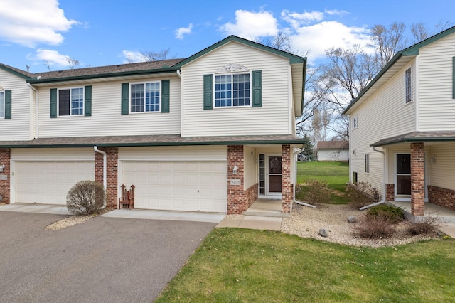 view of front of house featuring a front yard, an attached garage, aphalt driveway, and brick siding