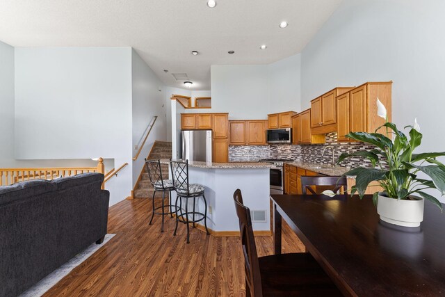 kitchen featuring a breakfast bar area, stainless steel appliances, a center island, wood finished floors, and backsplash