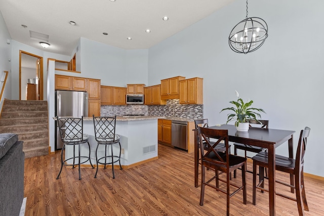 kitchen featuring an inviting chandelier, decorative backsplash, stainless steel appliances, light wood-style floors, and visible vents