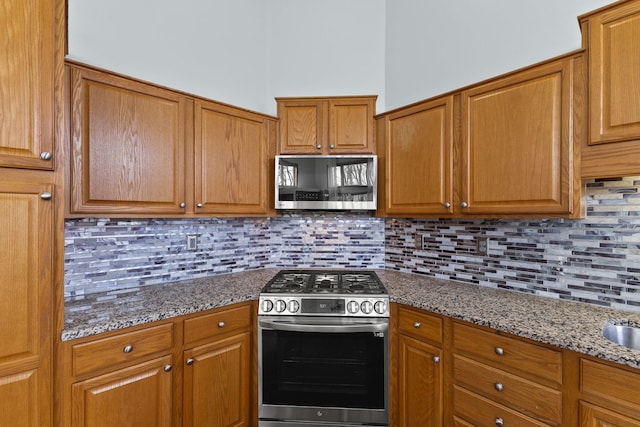 kitchen featuring dark stone countertops, brown cabinetry, appliances with stainless steel finishes, and decorative backsplash