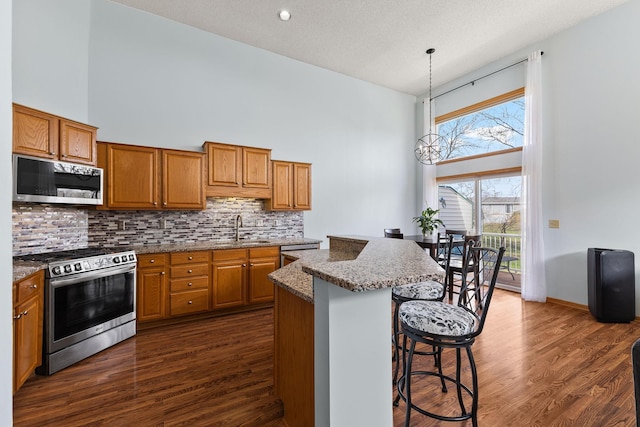 kitchen with brown cabinets, a high ceiling, appliances with stainless steel finishes, and a sink