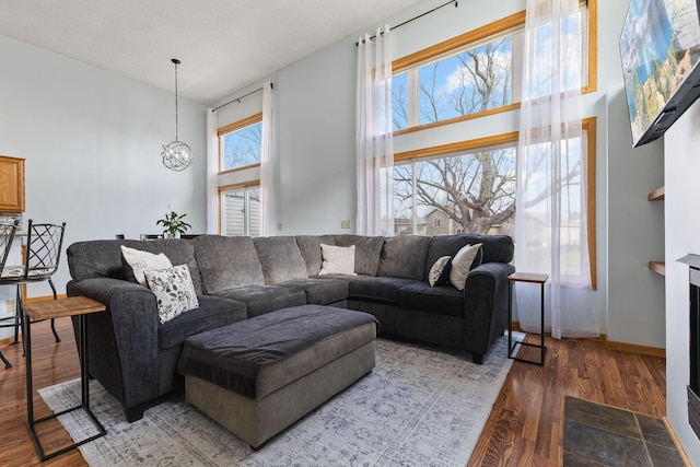 living area featuring wood finished floors, a high ceiling, a notable chandelier, and baseboards