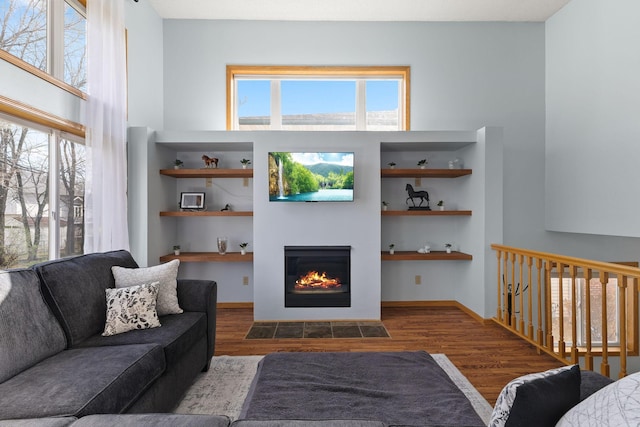living room featuring plenty of natural light, built in features, wood finished floors, and a glass covered fireplace