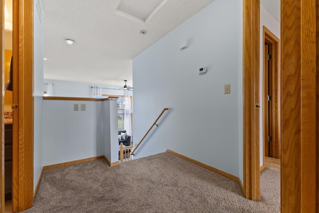 hall featuring attic access, an upstairs landing, carpet flooring, and baseboards