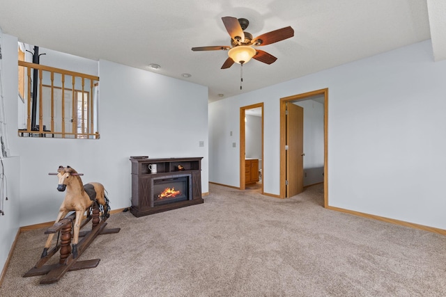 living room featuring carpet, ceiling fan, a glass covered fireplace, and baseboards
