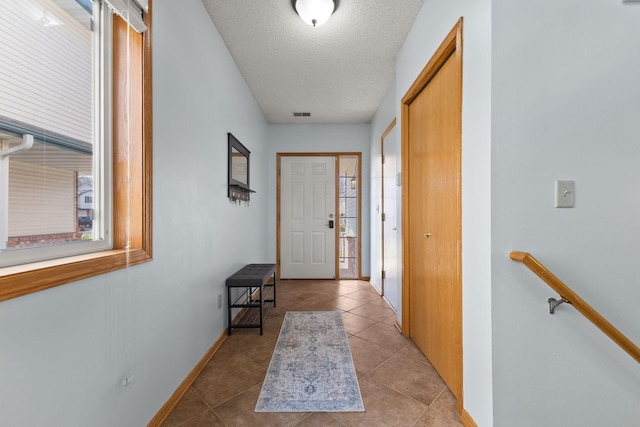 doorway to outside with a textured ceiling, visible vents, plenty of natural light, and baseboards
