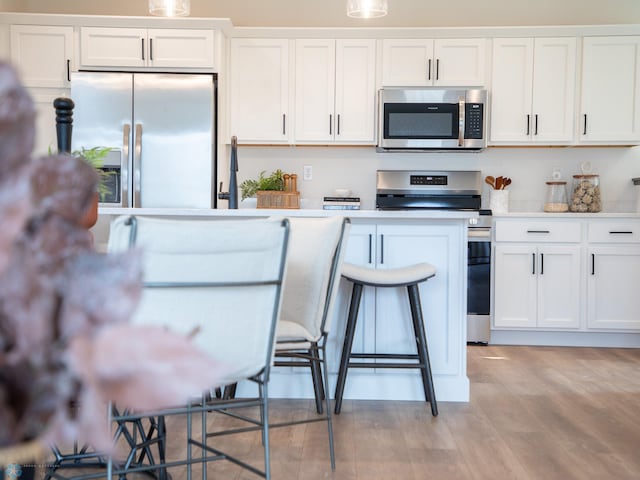 kitchen featuring light wood finished floors, light countertops, a kitchen breakfast bar, stainless steel appliances, and white cabinetry
