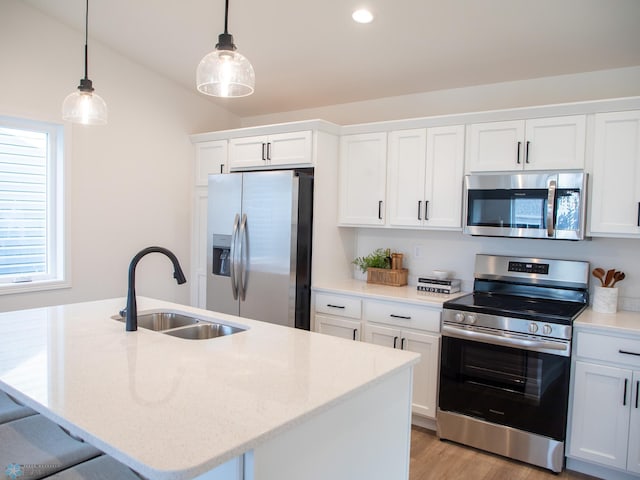 kitchen with pendant lighting, a kitchen island with sink, white cabinetry, a sink, and appliances with stainless steel finishes