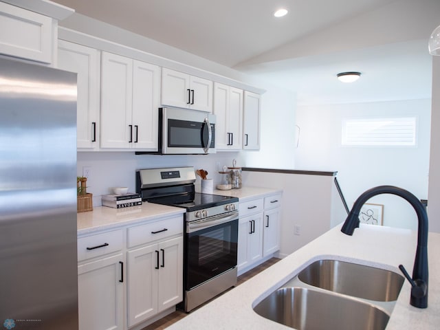 kitchen with white cabinets, stainless steel appliances, vaulted ceiling, and a sink