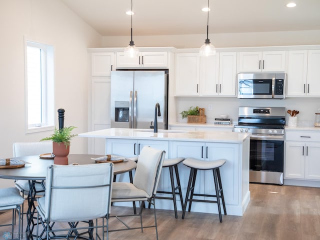 kitchen featuring a center island with sink, a kitchen bar, light countertops, a sink, and stainless steel appliances