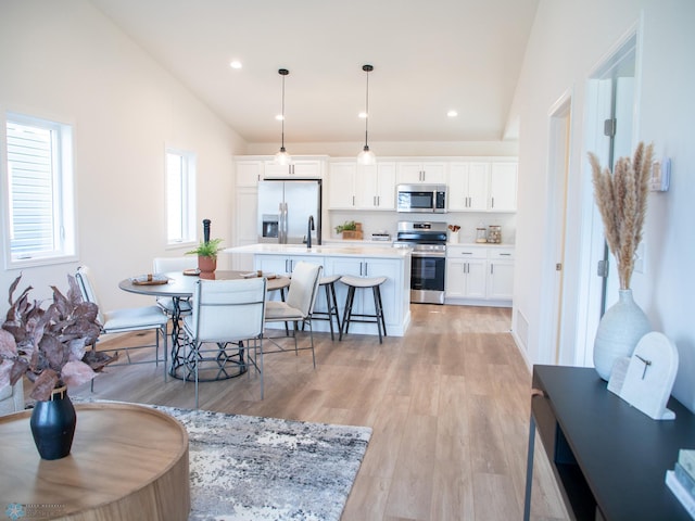 interior space featuring white cabinets, a kitchen island with sink, light countertops, stainless steel appliances, and vaulted ceiling