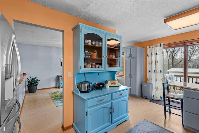 13229 Fremont Ave, Zimmerman, MN 55398 - kitchen with stainless steel fridge with ice dispenser, a textured ceiling, light wood finished floors, blue cabinetry, and glass insert cabinets