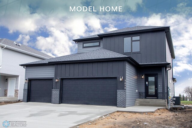 view of front of property featuring board and batten siding, driveway, roof with shingles, central air condition unit, and an attached garage