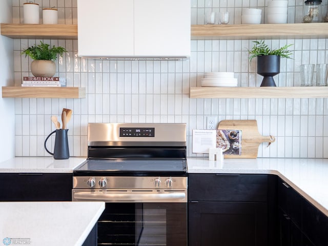 kitchen featuring open shelves, stainless steel range with electric stovetop, light countertops, dark cabinetry, and backsplash