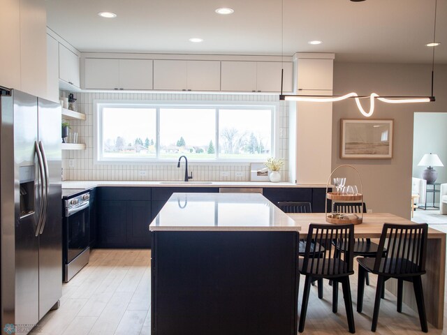 kitchen with appliances with stainless steel finishes, tasteful backsplash, light wood-type flooring, a sink, and light countertops