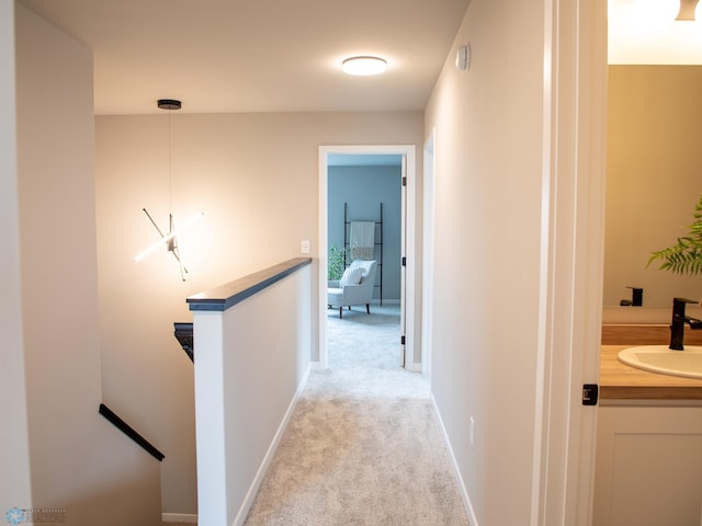 corridor featuring light colored carpet, baseboards, an upstairs landing, and a sink