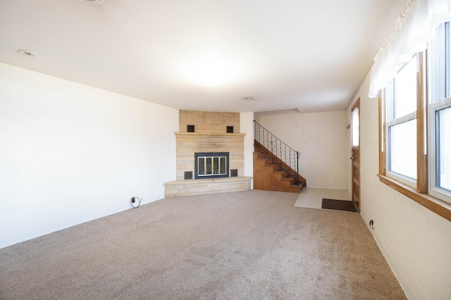 unfurnished living room featuring a stone fireplace, carpet flooring, and stairway