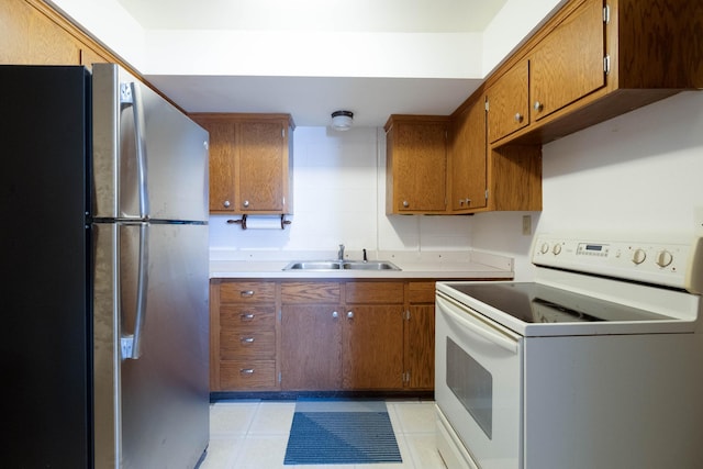 kitchen with freestanding refrigerator, brown cabinetry, white electric range, and a sink