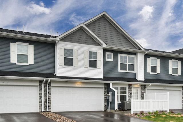 townhome / multi-family property with fence, stone siding, a garage, central air condition unit, and driveway