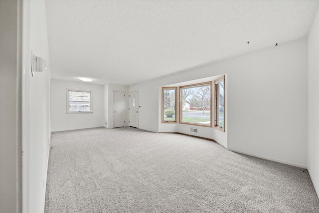 unfurnished room featuring carpet flooring, a textured ceiling, visible vents, and baseboards