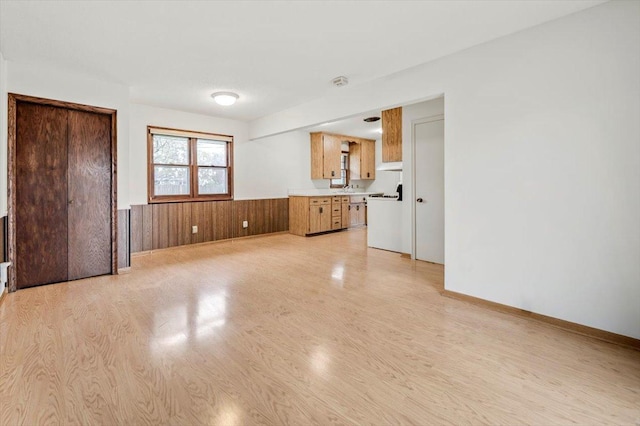 unfurnished living room with wood walls, wainscoting, and light wood-style flooring