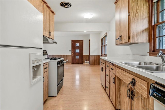kitchen featuring a sink, freestanding refrigerator, a wainscoted wall, gas range, and under cabinet range hood