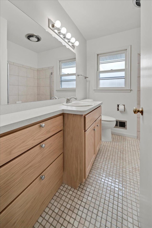 bathroom with toilet, vanity, visible vents, tile patterned floors, and a tile shower