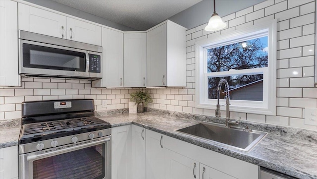 kitchen with a sink, decorative backsplash, pendant lighting, white cabinets, and appliances with stainless steel finishes