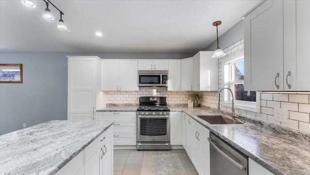 kitchen featuring stainless steel appliances, backsplash, a sink, hanging light fixtures, and white cabinetry