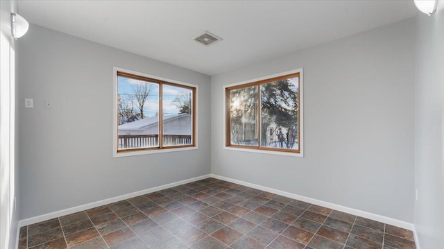 spare room with stone finish flooring, baseboards, and visible vents
