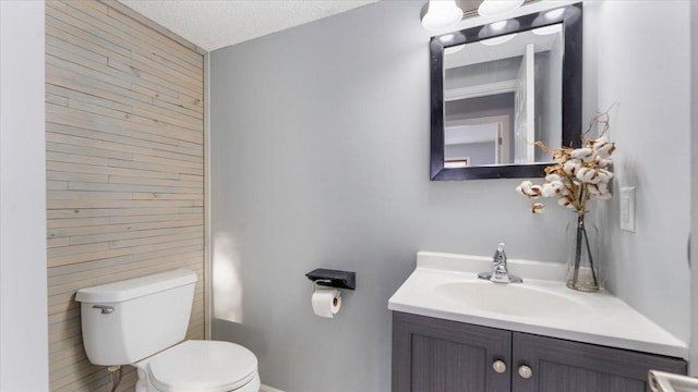 bathroom with wooden walls, a textured ceiling, toilet, and vanity