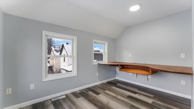 interior space with built in desk, vaulted ceiling, visible vents, dark wood-type flooring, and baseboards