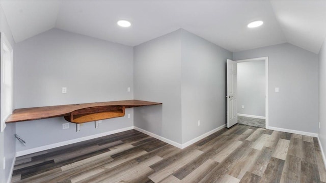 unfurnished office featuring lofted ceiling, wood finished floors, and built in desk