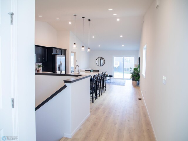 corridor with lofted ceiling, light wood-style floors, baseboards, recessed lighting, and a sink