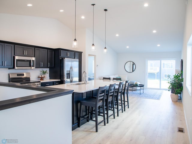 kitchen featuring a breakfast bar area, visible vents, a sink, high vaulted ceiling, and stainless steel appliances
