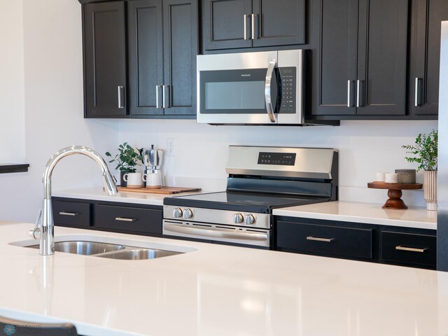 kitchen featuring a sink, appliances with stainless steel finishes, dark cabinetry, and light countertops