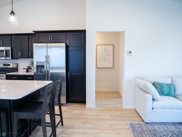 kitchen featuring appliances with stainless steel finishes, light wood-style floors, light countertops, baseboards, and a kitchen bar