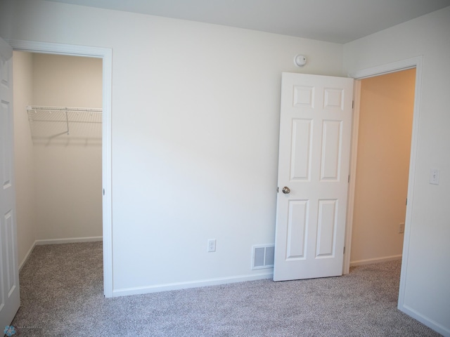 unfurnished bedroom with a walk in closet, visible vents, baseboards, a closet, and carpet flooring