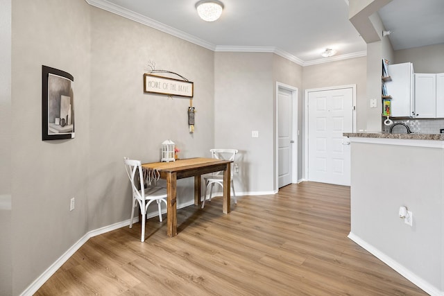 dining area with light wood-style floors, ornamental molding, and baseboards