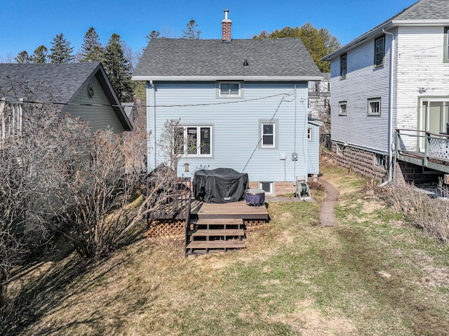 back of house with a lawn, roof with shingles, a chimney, and a deck