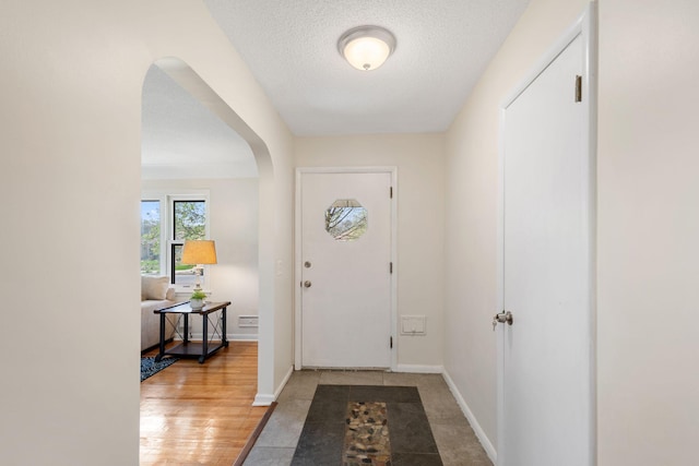 doorway featuring baseboards, arched walkways, and a textured ceiling