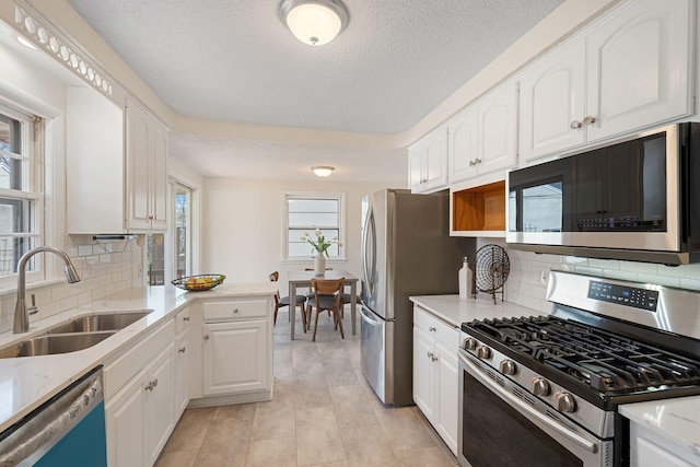 kitchen with white cabinets, a sink, a textured ceiling, stainless steel appliances, and tasteful backsplash