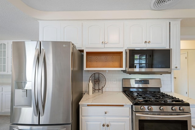 kitchen featuring backsplash, stainless steel appliances, white cabinets, and light stone countertops