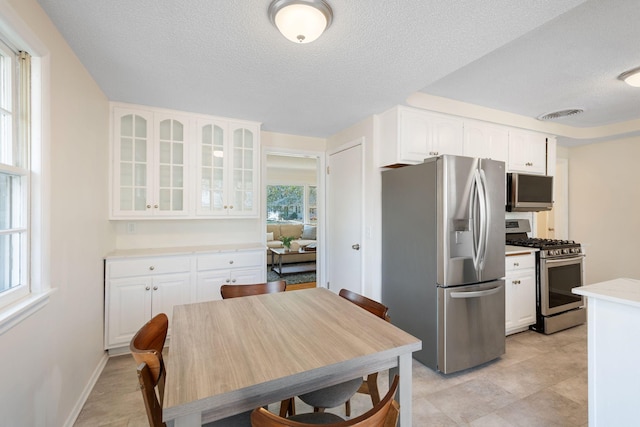 kitchen with visible vents, glass insert cabinets, a textured ceiling, white cabinetry, and appliances with stainless steel finishes