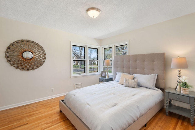 bedroom featuring baseboards, a textured ceiling, and wood finished floors
