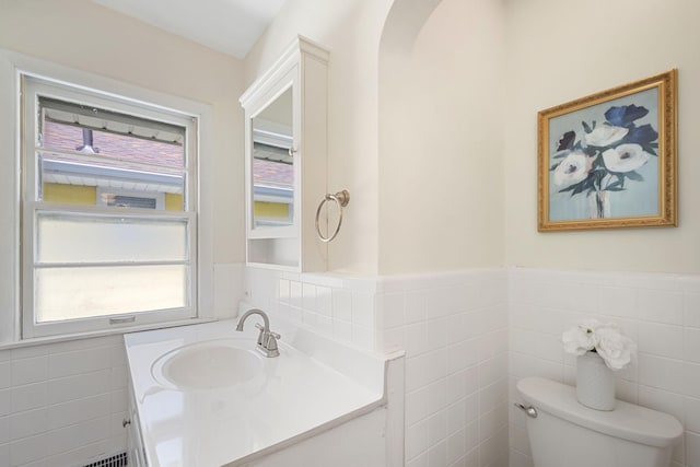 half bathroom with toilet, tile walls, wainscoting, and vanity
