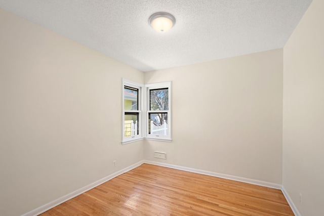 unfurnished room with light wood-type flooring, a textured ceiling, and baseboards