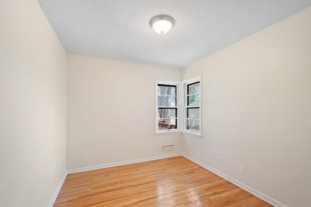 spare room featuring light wood-type flooring, a textured ceiling, and baseboards
