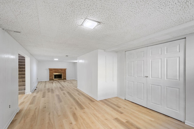 below grade area featuring stairs, baseboards, a brick fireplace, and light wood-type flooring
